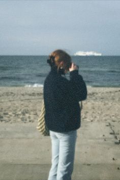 a woman is standing on the beach talking on her cell phone and looking at the ocean