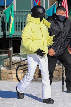 two people walking in the snow wearing skis and jackets with masks on their faces