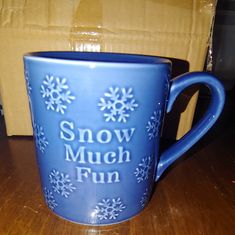 a blue coffee mug with snow much fun written on it sitting on a wooden table