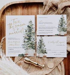 the wedding stationery is laid out on a wooden tray with gold calligraphy and greenery