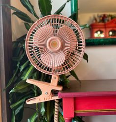 a pink fan sitting on top of a red table next to a green potted plant