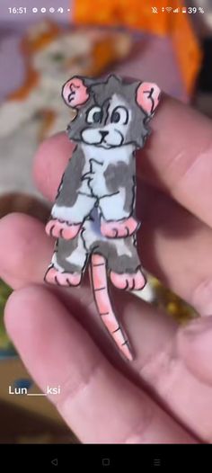 a hand holding a small sticker with a cat on it's back and eyes