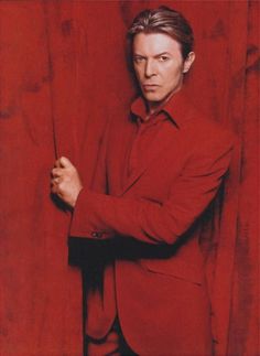 a man in a red suit and tie leaning against a wall with his arms crossed