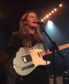 a woman singing into a microphone while holding a guitar