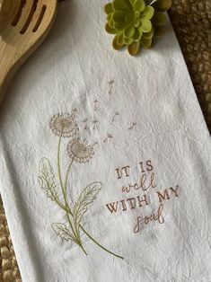 an embroidered tea towel with the words it is well with my soul on it next to a wooden spoon