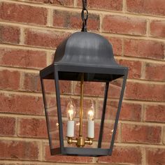 a light hanging from the side of a brick wall with two candles in front of it