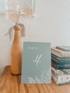 a table number sitting on top of a wooden table next to a vase filled with flowers