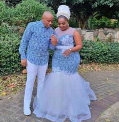 two people standing next to each other in front of some bushes and trees, one wearing a blue dress