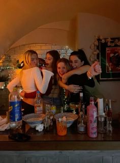 four women are posing for the camera in front of a counter with bottles and glasses on it