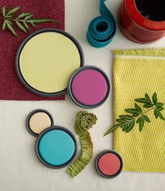 various paints and brushes on a table next to a potted plant, napkins, and other items