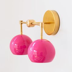 two pink balls are hanging from a gold hook on a white wall with a round light fixture