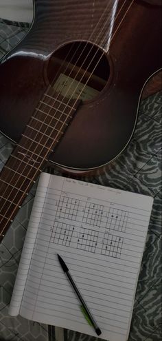 a guitar, notebook and pen sitting on top of a bed