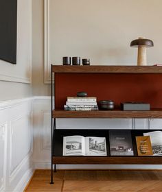 a shelf with books and magazines on it in the corner of a white walled room