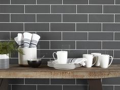 a table topped with plates and cups filled with food next to a wall covered in grey tiles