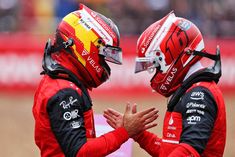 two men in red racing suits standing next to each other with helmets on their heads