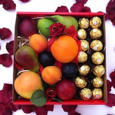 a box filled with assorted fruit and chocolates on top of red flowers in front of a white background