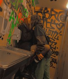 a man and woman standing in front of a sink with graffiti on the wall behind them