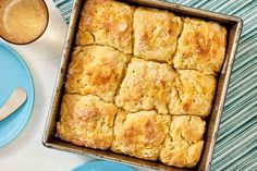 a pan filled with biscuits next to two plates and spoons on a blue table cloth