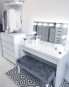 a white dressing table with lights on it and a bench in front of the mirror