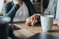 two people sitting at a table holding hands with one person's hand over the other