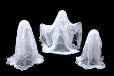 three white plastic ghost figures on a black surface with veils over their heads and hands