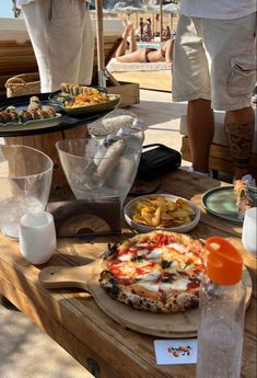 there is a pizza and other food on the table at this outdoor party with people in the background