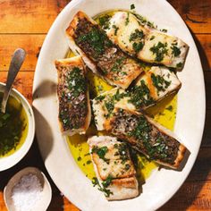 fish fillets on a plate with lemon and parsley garnish next to a small bowl of pesto