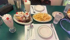 a table topped with plates and glasses filled with desserts next to cups full of milkshakes