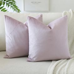 two lavender pillows on a white couch with a green plant in the corner behind them