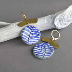 Ethnic inspired brass earrings embellished with a unique glass disc with cobalt blue stripes. The glass disc is hand painted with vitreous enamels fused permanently into the glass. The decor will never fade or disappear. Choose the color in the drop-down box. Length: 50 millimeters (2 inches) Width: 27 millimeters (1 inch) Materials: Raw brass huggie hoop (nickel and lead free) Recycled fused glass bead Boho earrings, elegant and chic for when you need that little extra to set you apart from the Blue Brass Jewelry With Ear Wire, Unique Blue Brass Jewelry, Artisan Blue Hand Painted Jewelry, Bohemian Hand Painted Brass Jewelry, Bohemian Hand Painted Brass Earrings, Blue Enamel Earrings With Artistic Design, Hand-painted Blue Dangle Jewelry, Artisan Blue Brass Earrings, Handmade Blue Glass Earrings