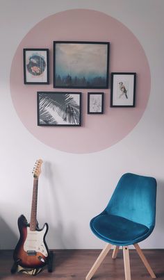 a blue chair sitting next to a guitar on top of a hard wood floor in front of a pink wall