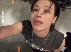 a woman with black hair wearing a gray shirt and silver necklace is taking a selfie