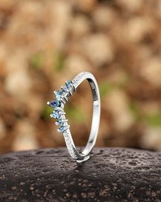 a white gold ring with blue topazte and diamonds on a rock in front of some rocks