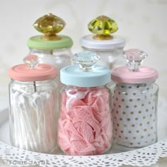 four glass jars with different colored lids on a lace doily and white doily