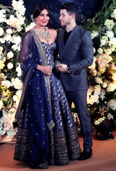 two people standing next to each other in front of a floral wall with white and blue flowers