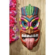 a colorful mask hanging on the side of a wall with flowers in front of it