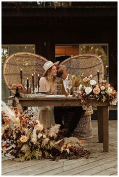 a man and woman are sitting at a table with flowers on it, surrounded by candles