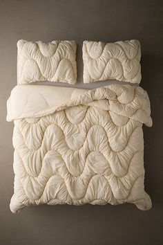 an unmade bed with two pillows and a white comforter on top of it