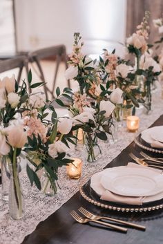 the table is set with white plates and flowers in vases, candles and napkins