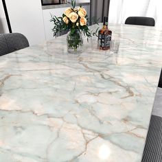 a marble dining table with flowers in a vase and bottles on the table top,