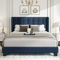 a bed with blue headboard and pillows in a white walled room next to two lamps on either side of the bed