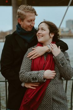 a man and woman standing next to each other near the water with their arms around each other