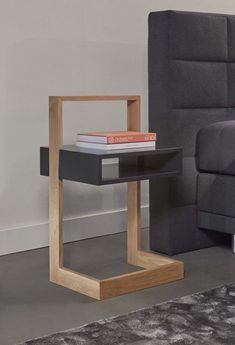 a black and wood end table with books on it in front of a gray couch