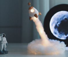 a toy rocket launching into the sky next to an astronaut figurine