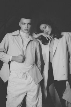 a man and woman standing next to each other in black and white photo by photographer