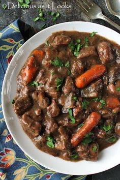 a white bowl filled with meat and carrots on top of a blue table cloth