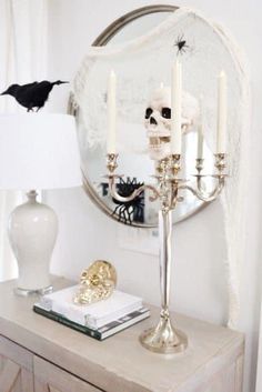 a white table topped with a mirror and two candles next to a skull head on top of a dresser