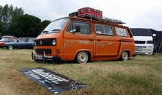 an orange van with luggage on top parked in a field next to other cars and tents