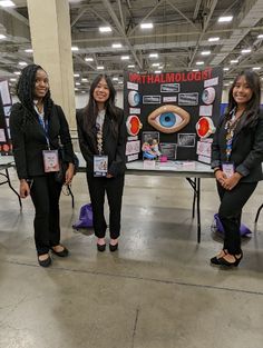 three women standing in front of a table with an eye poster on it and one woman holding up a sign