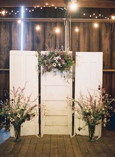 an old door is decorated with flowers and greenery in front of some lights on the wall